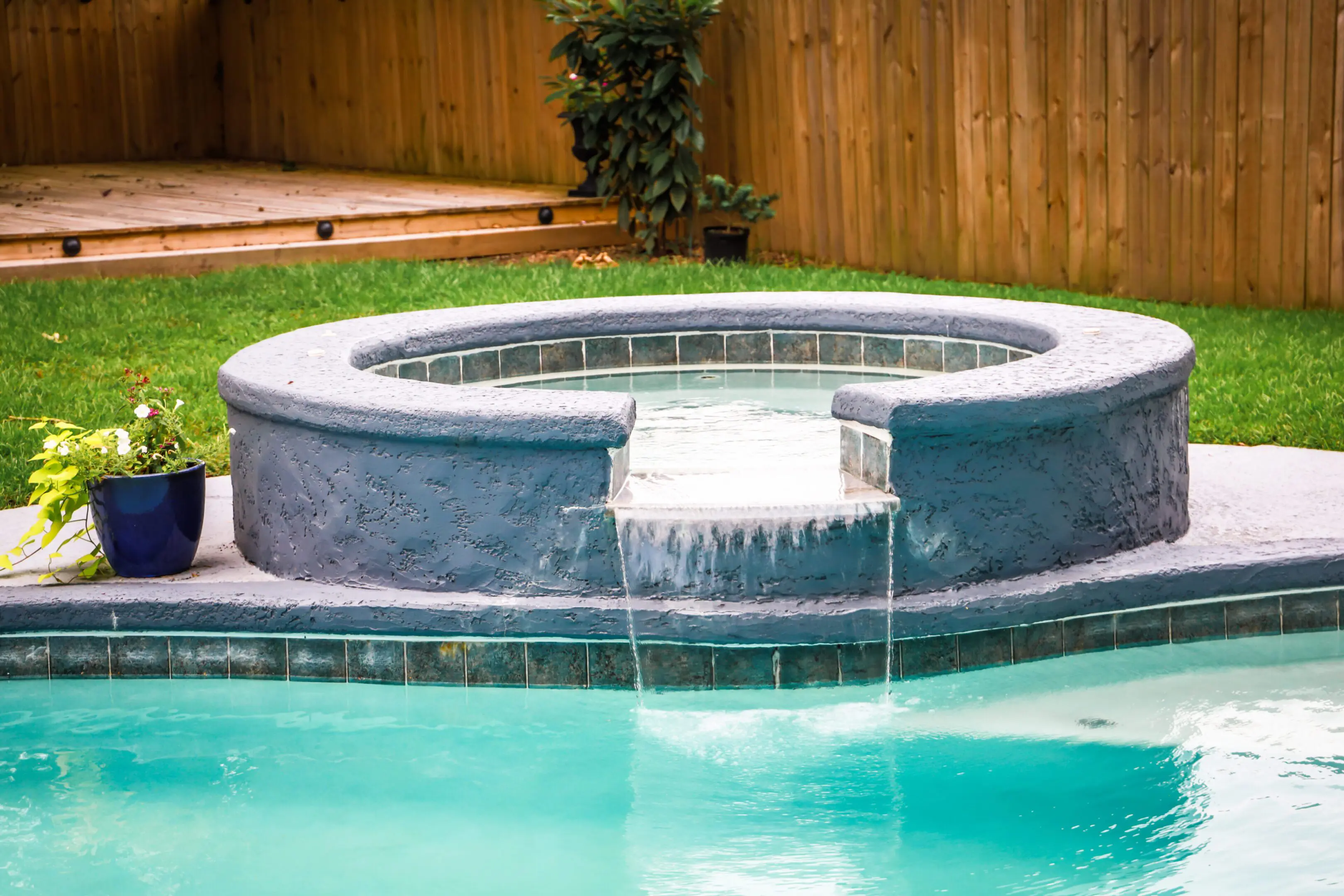 A Hot Tub hot tub next to a large freeform swimming pool with a waterfall water feature running.